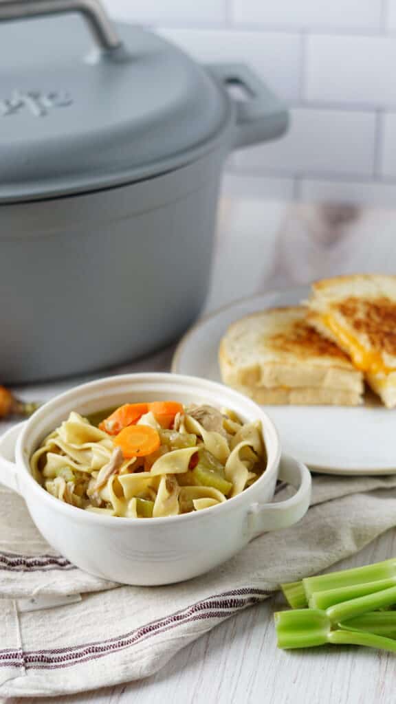 turkey noodle soup in bowl with grilled cheese and pampered chef dutch oven cooking vessel