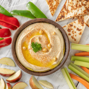 Hummus in a bowl with pita bread and vegetables surrounding it